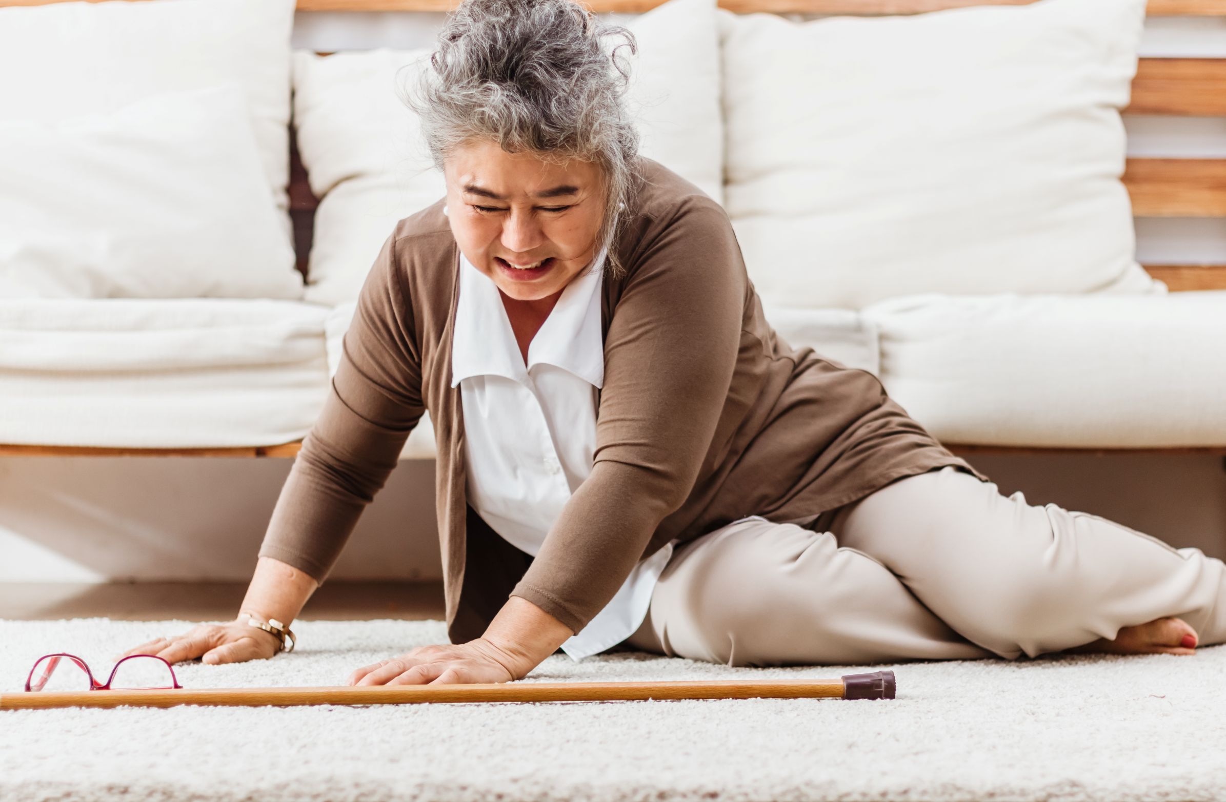 Senior woman who has fallen on the floor of her home, with her eyeglasses and cane on the ground next to her.